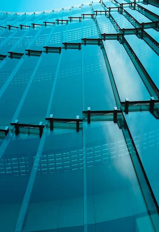Vista contrapicada de una fachada de vidrio estructural en tonos azul turquesa con herrajes metálicos.